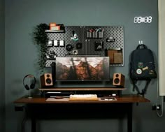 a desk with a monitor, keyboard and headphones on it in front of a green wall