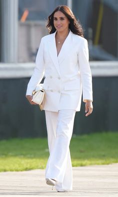 a woman in a white suit walking down the street with a purse on her hand