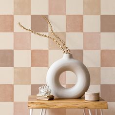 a white vase sitting on top of a wooden table next to a wall with checkered walls