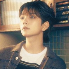 a young man standing in front of a wall with books on the shelf behind him