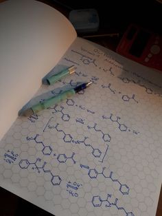 two pens sitting on top of a sheet of paper with chemical symbols drawn on it