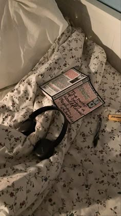 an unmade bed with a book and headphones laying on it's side