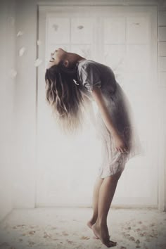 a woman standing in front of a window with her hair blowing in the wind and looking up