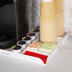 the coffee maker is sitting next to some cups and saucers on a white tray