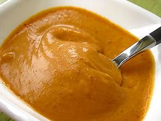 a spoon is in a bowl full of orange colored sauce on a green tablecloth