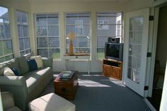 a living room filled with furniture and windows next to a tv on top of a wooden table