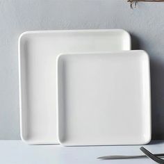 two white square plates sitting on top of a table next to a knife and fork