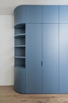 an empty room with blue cupboards and wood flooring on the side, in front of a white wall