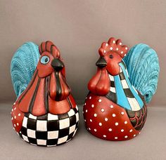 two ceramic rooster figurines sitting next to each other on a gray tablecloth