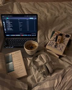 an open laptop computer sitting on top of a bed next to books and headphones