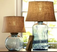 two glass vases sitting on top of a table with a lamp next to them