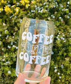 someone is holding up a glass with coffee on it in front of some bushes and flowers