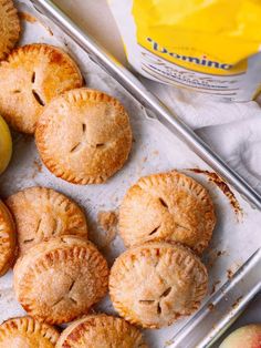 apple pies on a baking sheet next to some sliced apples and a can of orange juice