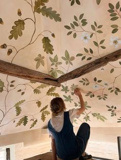 a woman is sitting on the floor and painting a ceiling with flowers painted on it