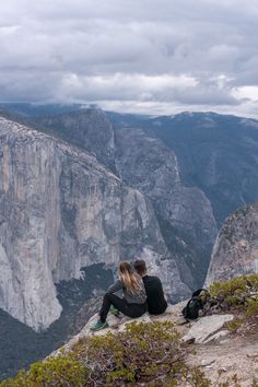 two people sitting on the edge of a cliff