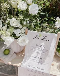 there is a menu on the table with white flowers and greenery in the background