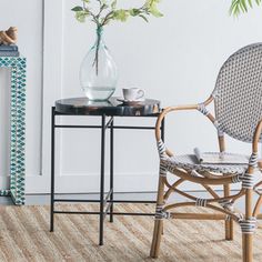 a wicker chair next to a table with a vase on it and a plant in the corner