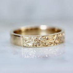 a gold wedding band with flowers and leaves engraved on the side, sitting on a white surface