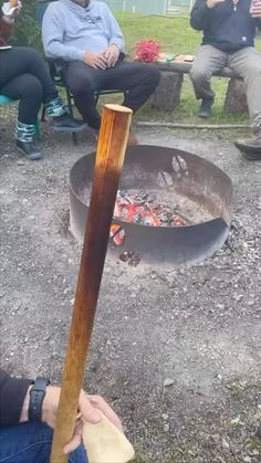 people sitting around an open fire pit in the middle of a park with one person holding a stick