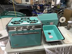 two stoves are sitting on a table in a garage, one is blue and the other is green