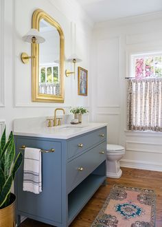 a bathroom with a blue vanity and gold framed mirror above it, along with a rug on the floor