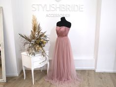 a dress is on display in front of a white table with a vase and mirror