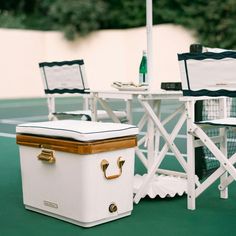 two chairs and a table on a tennis court with a cooler in the foreground