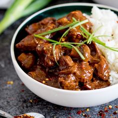 a white bowl filled with meat and rice on top of a black table next to chopsticks