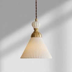 a white and gold colored light hanging from a ceiling fixture with a brown cord attached to it