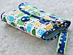 a blue and green owl print purse with two zippers on the side, sitting on a concrete surface