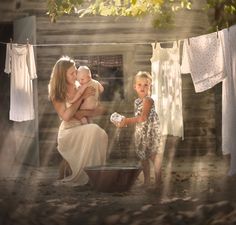 a woman holding a baby in her arms and washing clothes on a line with laundry hanging to dry