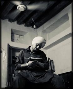 a man sitting in a chair looking at his cell phone while wearing a turban