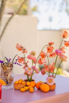 three vases filled with flowers and oranges sitting on top of a purple table