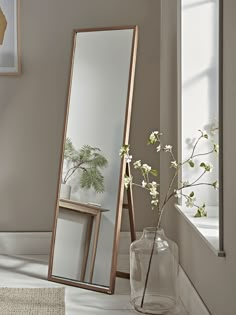 a mirror sitting on top of a floor next to a vase with flowers in it