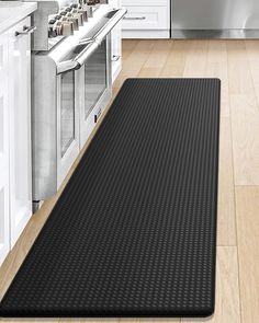 a kitchen with white cabinets and black mat on the floor in front of an oven