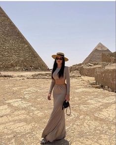 a woman standing in front of the giza pyramids wearing a hat and dress