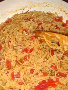 a pan filled with pasta and vegetables on top of a wooden spoon in the middle of it