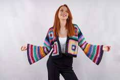 a woman with red hair is wearing a colorful crochet jacket and black pants