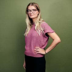 a woman wearing glasses standing in front of a green wall with her hands on her hips