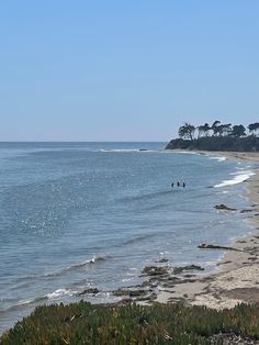 two people are walking on the beach near the water