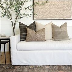 a white couch with several pillows on top of it next to a tree in a living room