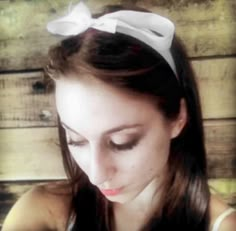 a woman with long brown hair wearing a blue and white bow headband looking down at her cell phone