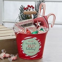 a red bucket filled with candy canes and other holiday treats sitting on top of a wooden table