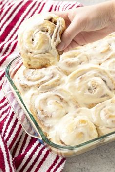 a person holding a cinnamon roll in a glass baking dish