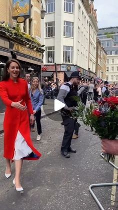 a woman in a red dress is walking down the street with flowers on her hand