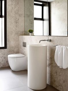 a white toilet sitting next to a sink in a bathroom under a window on top of a tiled floor