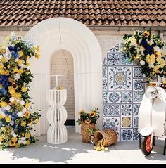 a white scooter parked next to a building with flowers on the wall and in front of it