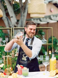 a man in an apron pours a drink at a table with lemons and other drinks