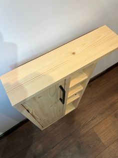 a wooden cabinet sitting on top of a hard wood floor next to a white wall