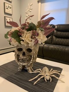 a skull vase with flowers in it sitting on top of a table next to a spider